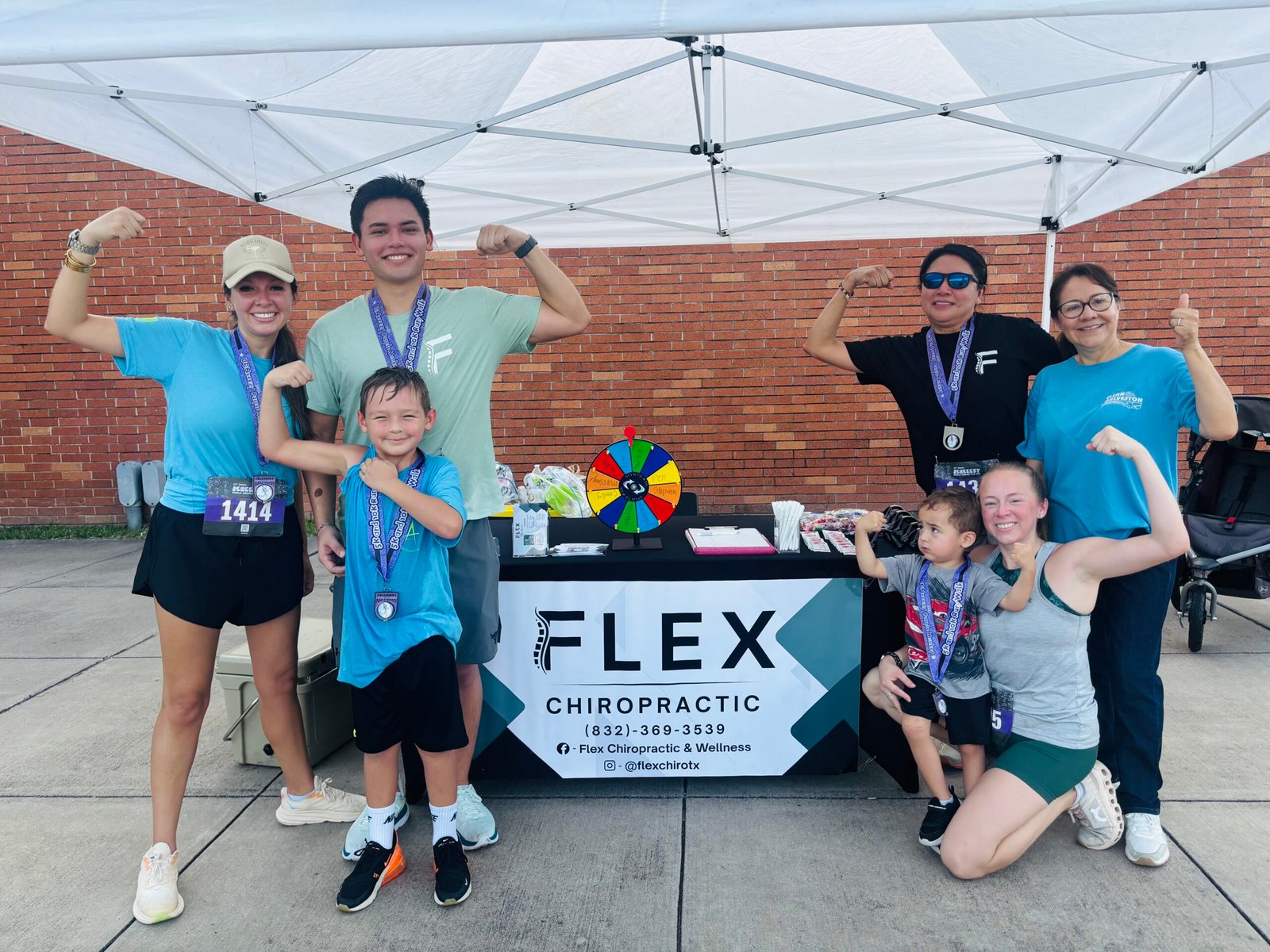 Flex Chiropractic team members smiling at their community 5K race booth.